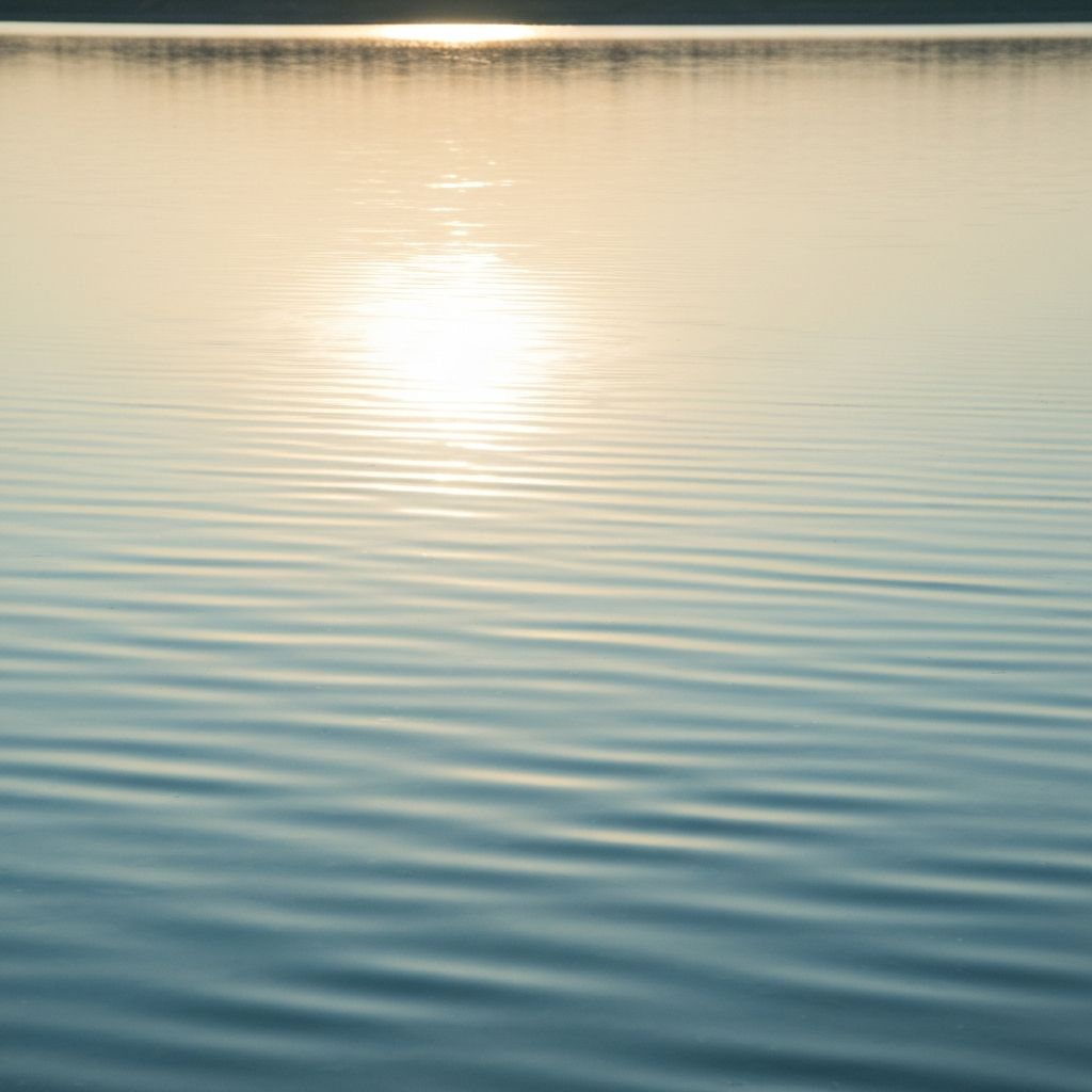 Superfície de água calma com reflexos suaves de luz natural, evocando serenidade e relaxamento visual, sem pessoas